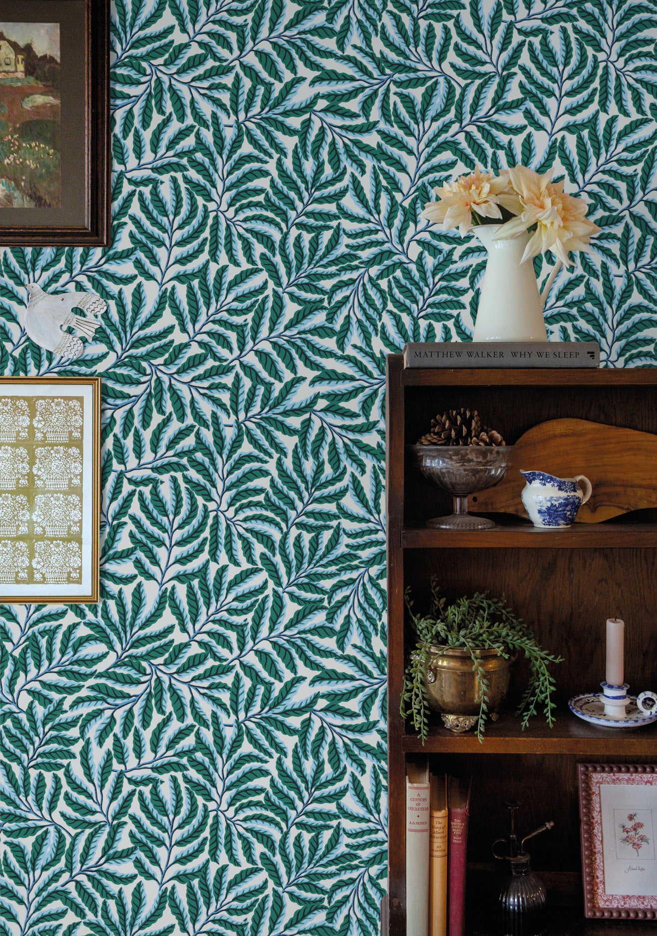 Room interior with green leaf-patterned wallpaper, bookshelf, and decorative items.