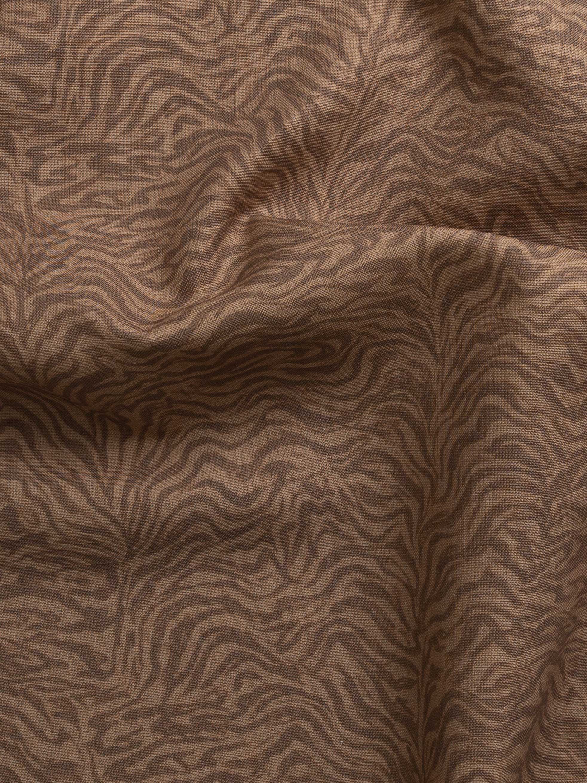 Detail of gently draped printed fabric with watercolor swirling stripe pattern in tonal warm terracotta brown.