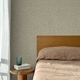Bed with tan linens and wooden headboard, wooden side table  with white book and green glass, white floor length curtain against a watercolor swirling stripe wallpaper in tonal sage green.