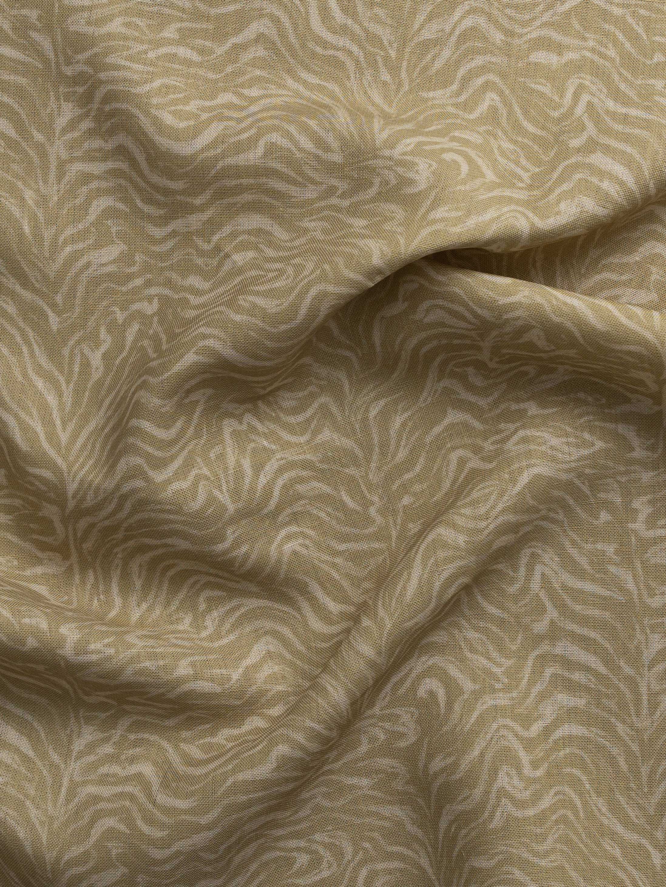 Detail of gently draped printed fabric with watercolor swirling stripe pattern in tonal muted ochre.
