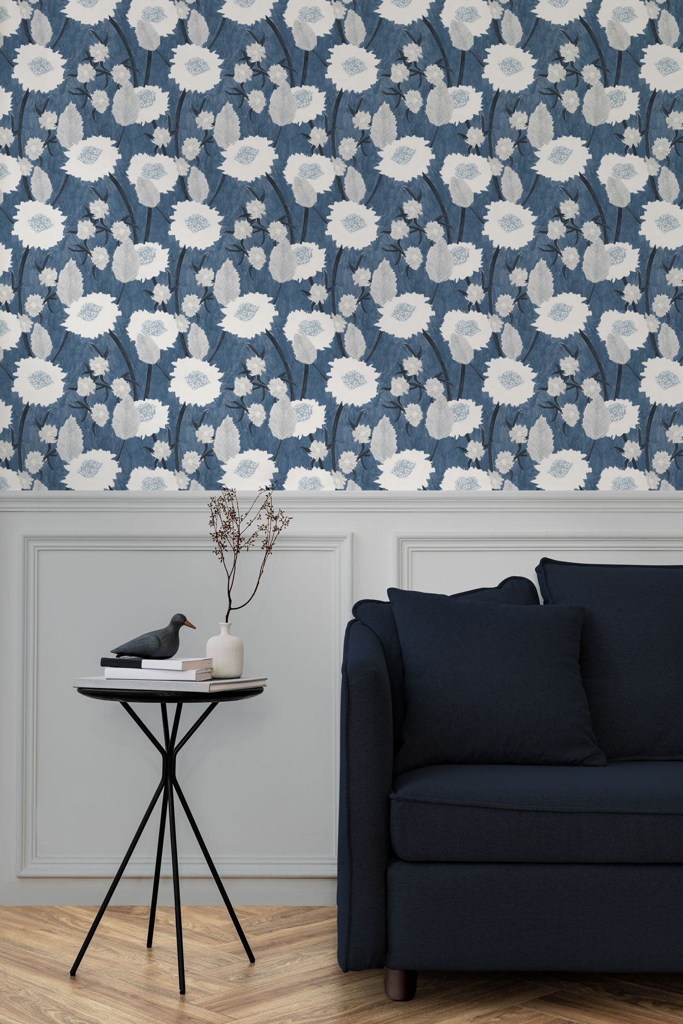 A couch and end table stand in front of a wall papered in a playful floral print in white, gray and navy.