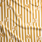 A close-up of a fabric surface with vertical mustard yellow and off-white stripes and repeated small daisy floral motifs.