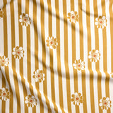 A close-up of a fabric surface with vertical mustard yellow and off-white stripes and repeated small daisy floral motifs.