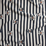 A close-up of a fabric pattern featuring vertical navy blue and off-white stripes with small daisy-like flowers in navy, white, and orange.