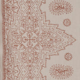 Detail of fabric in a dense paisley border print in rust on a tan field.