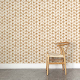 A wooden chair stands in front of a wall papered in a painterly lattice print in brown on a cream field.