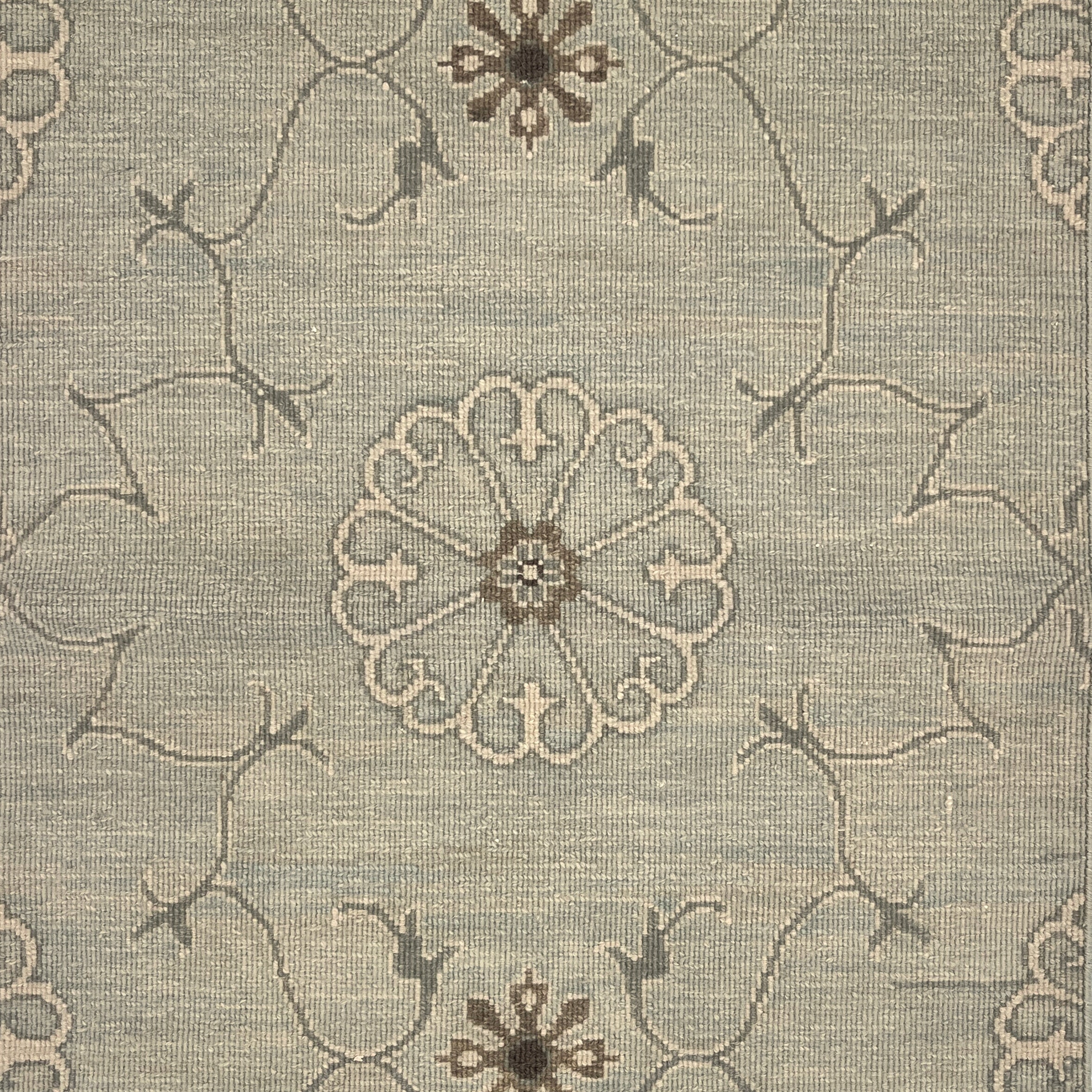 Close up of hand woven rug in a floral filigree pattern in grey, brown and cream on a grey-blue field.