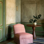 Pink chair in a room with green walls, a wooden table, and a plant.