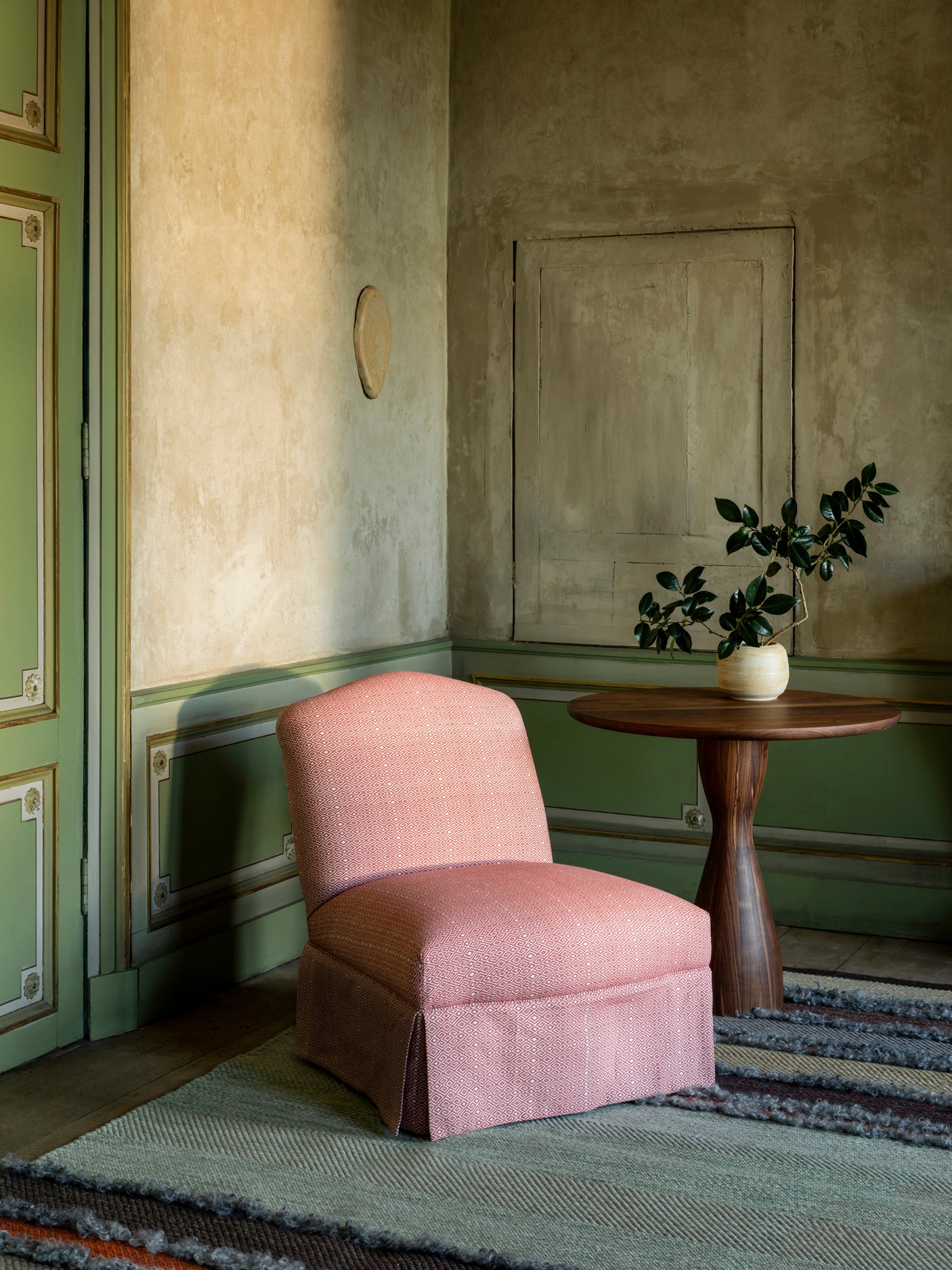 Pink chair in a room with green walls, a wooden table, and a plant.