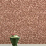A green wooden stool with books and a mug against botanical lace patterned wallpaper in terracotta pink.