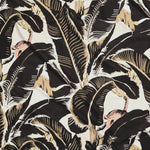 Close up of gently draped printed linen with bold banana leaf in shades of black, tan and light pink on white.