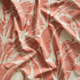 Close up of gently draped printed linen with bold high contrast tropical banana leaf pattern in clay pink on beige.