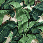 Close up of gently draped printed linen with bold banana leaf in shades of green and brown on white.