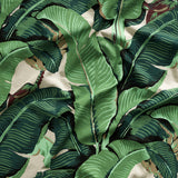 Close up of gently draped printed linen with bold banana leaf in shades of green and brown on white.