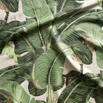 Close up of gently draped woven Indoor-Outdoor fabric with bold banana leaf in shades of green and tan on cream. 