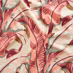 Close up of gently draped printed linen with bold banana leaf in shades of coral pink, magenta, grey and tan on cream,