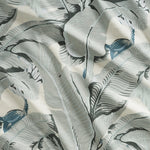 Close up of gently draped printed linen with bold banana leaf in shades of grey and steel blue on white.
