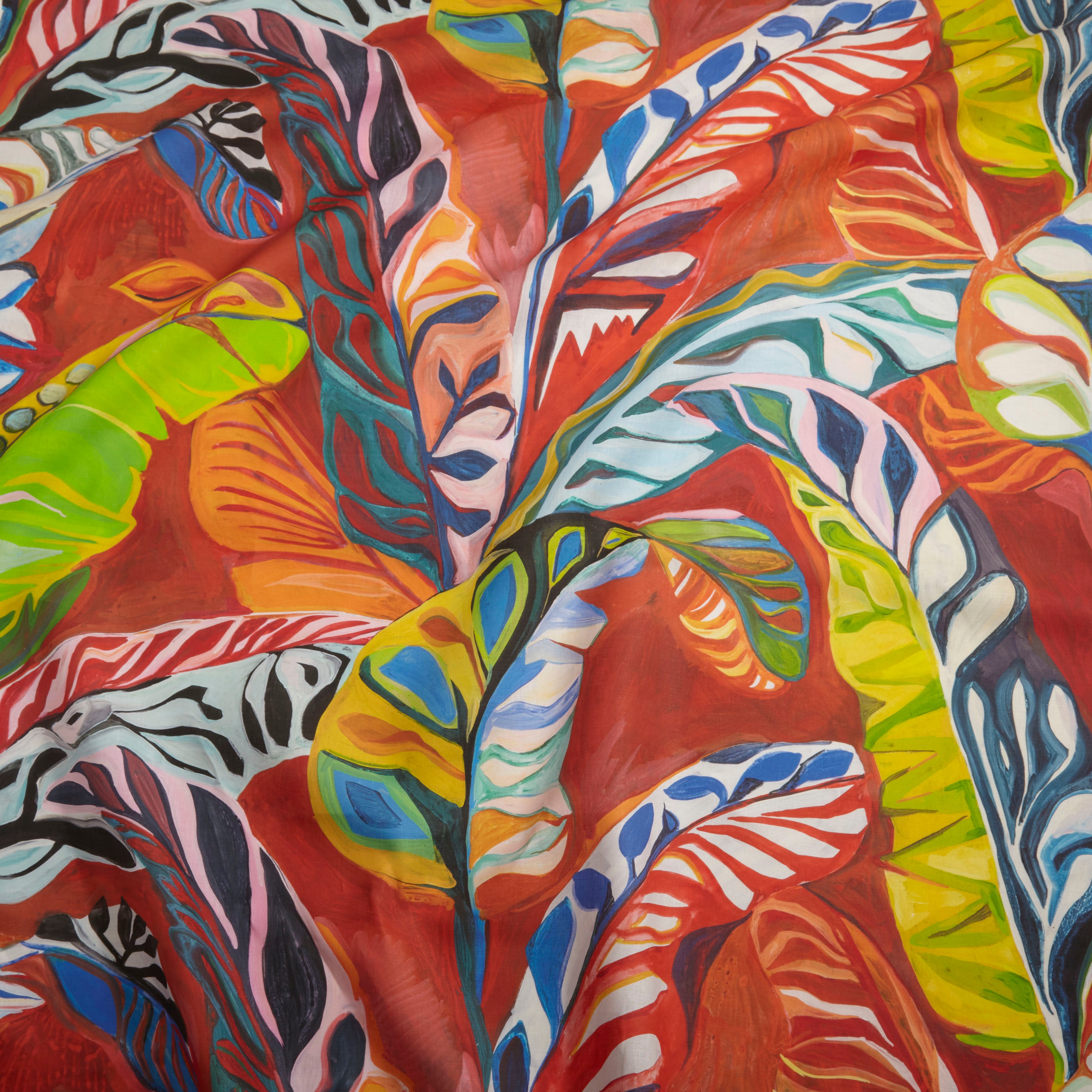 Close up of gently draped printed linen with expressive painterly banana-leaf pattern in red, yellow, green, pink and blue on a red field. 