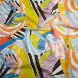 Close up of gently draped printed linen with an abstract striped banana-leaf pattern in yellow, orange, blue, purple and black and white. 