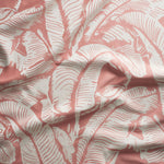 Close up of gently draped woven Indoor-Outdoor fabric with bold banana leaf pattern in white on coral pink.