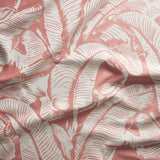 Close up of gently draped woven Indoor-Outdoor fabric with bold banana leaf pattern in white on coral pink.
