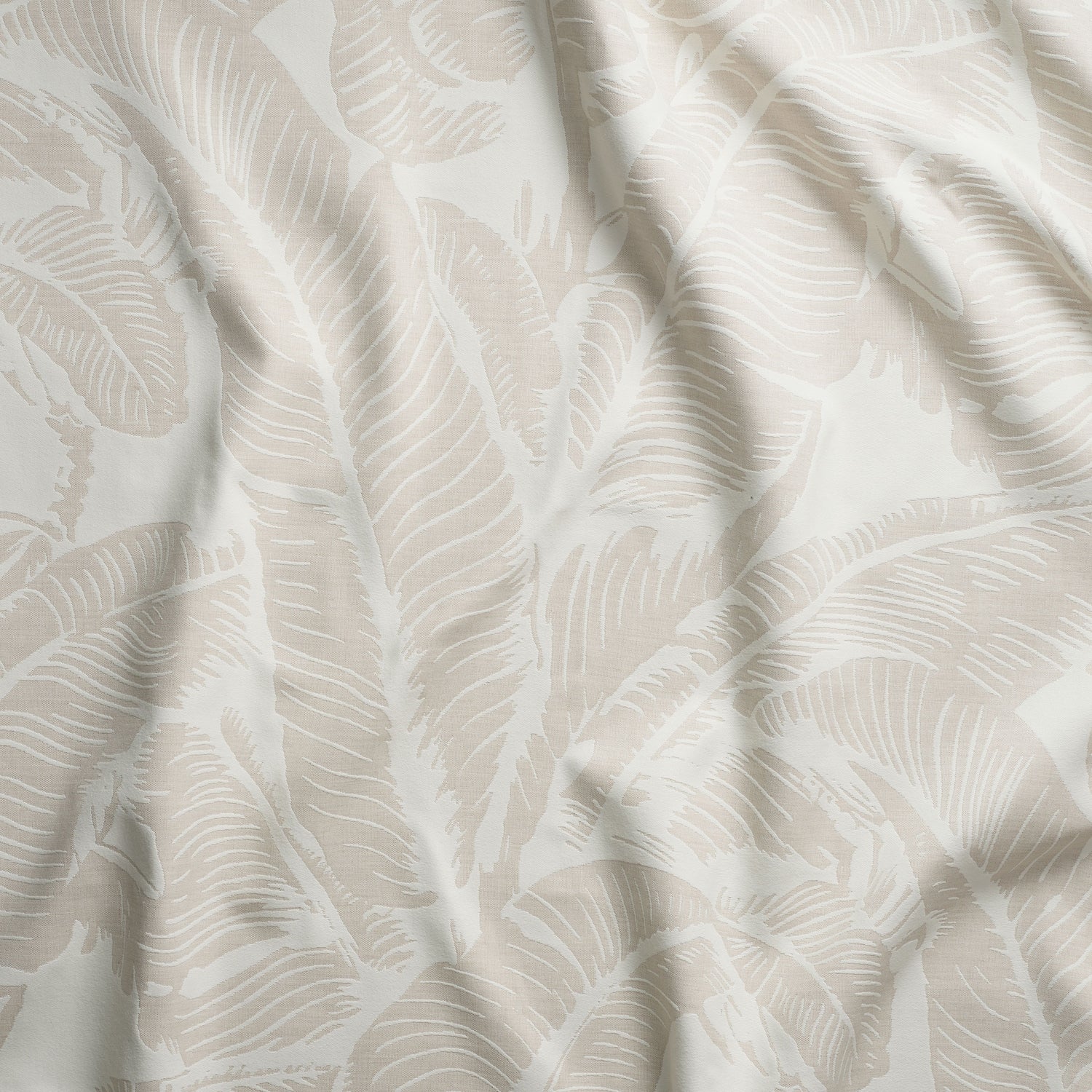 Close up of gently draped woven Indoor-Outdoor fabric with bold banana leaf pattern in white on beige.