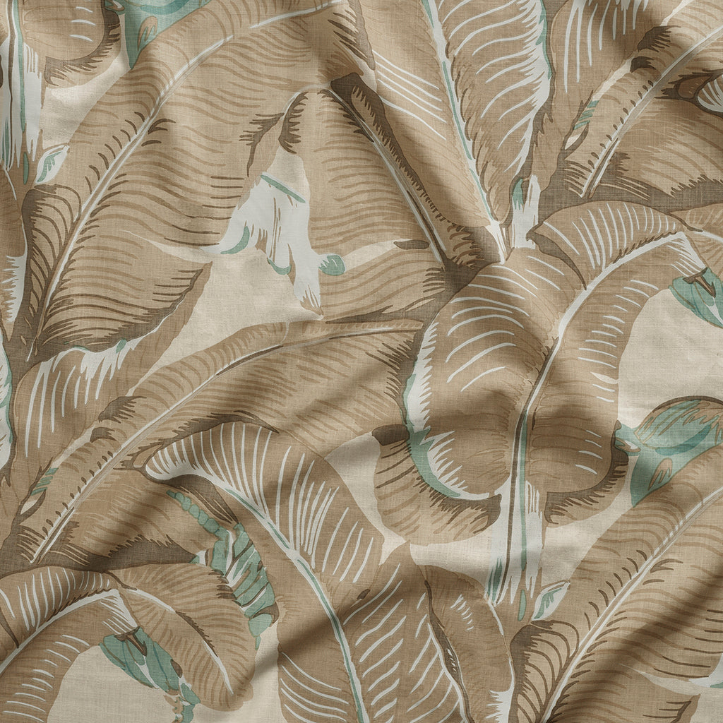 Close up of gently draped printed linen with bold banana leaf in shades of taupe and aqua blue on white.