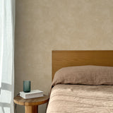 Bed with tan linens and wooden headboard, wooden side table  with white book and green glass, white floor length curtain against a white celestial dotted pattern on a tan background. 