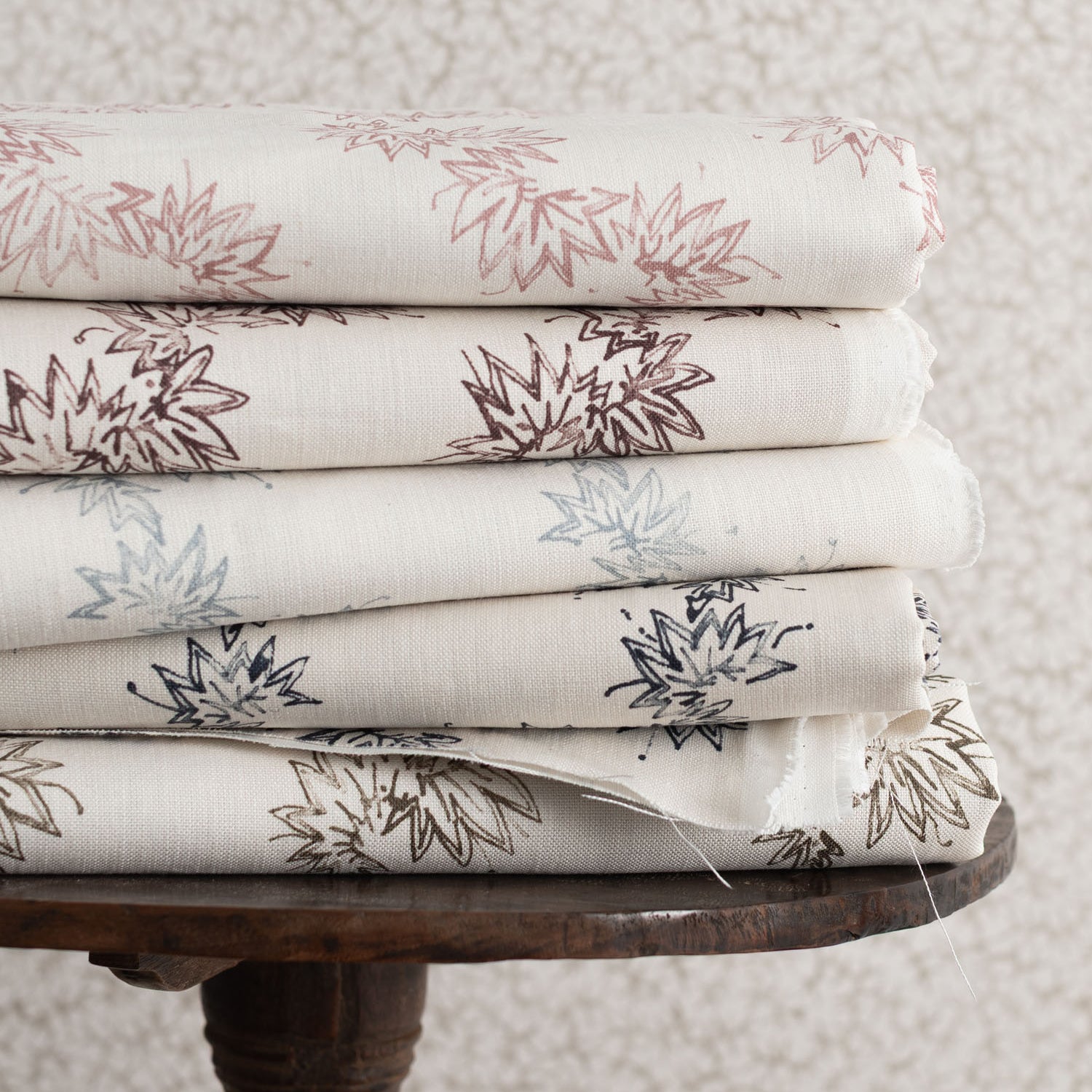Stack of folded fabric with floral patterns on a wooden table against a textured wall.