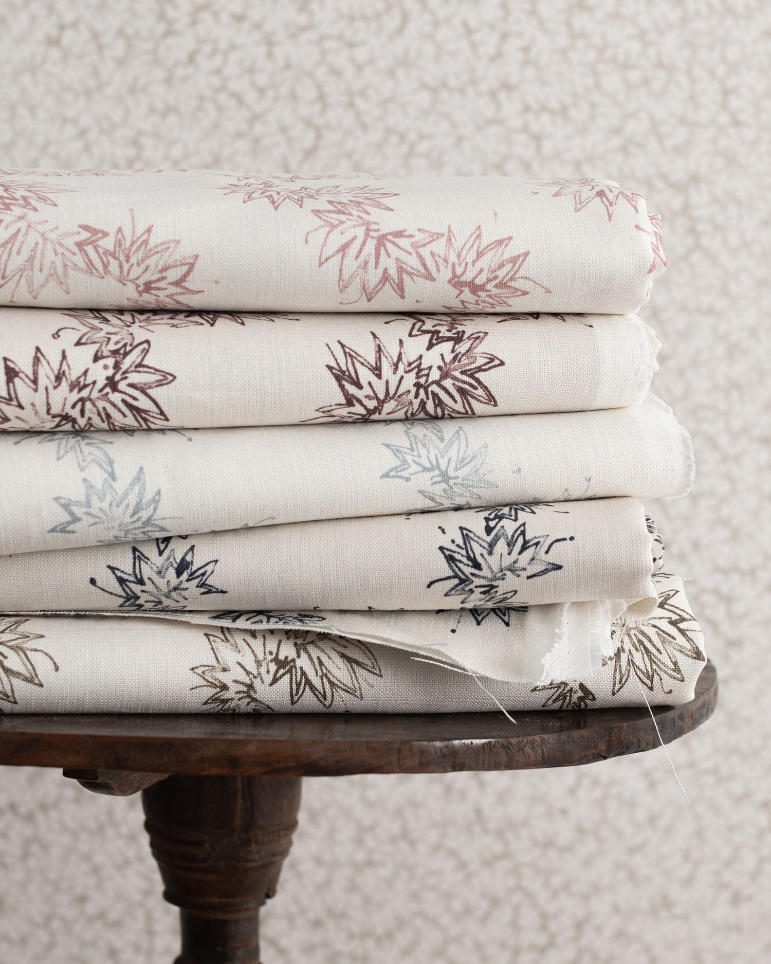 Stack of folded fabric with floral patterns on a wooden table against a textured wall.