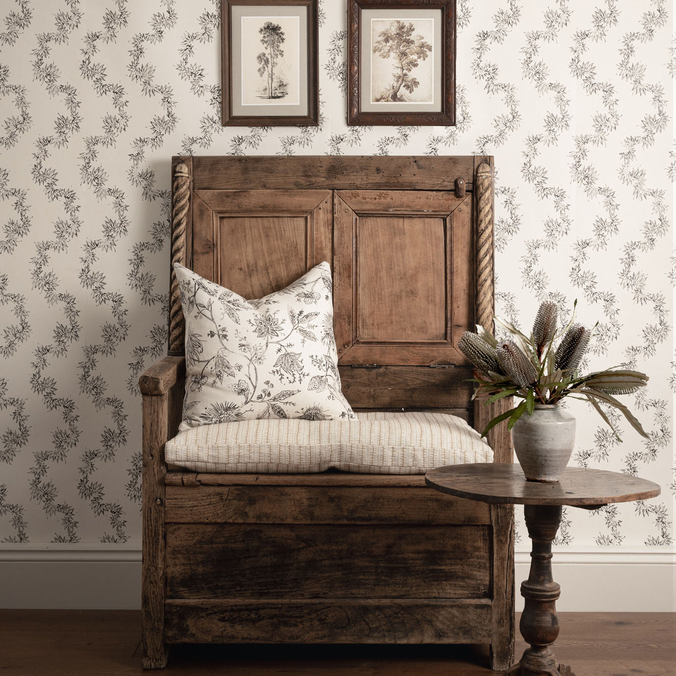 Wooden bench with floral cushion against a patterned wall with framed pictures.