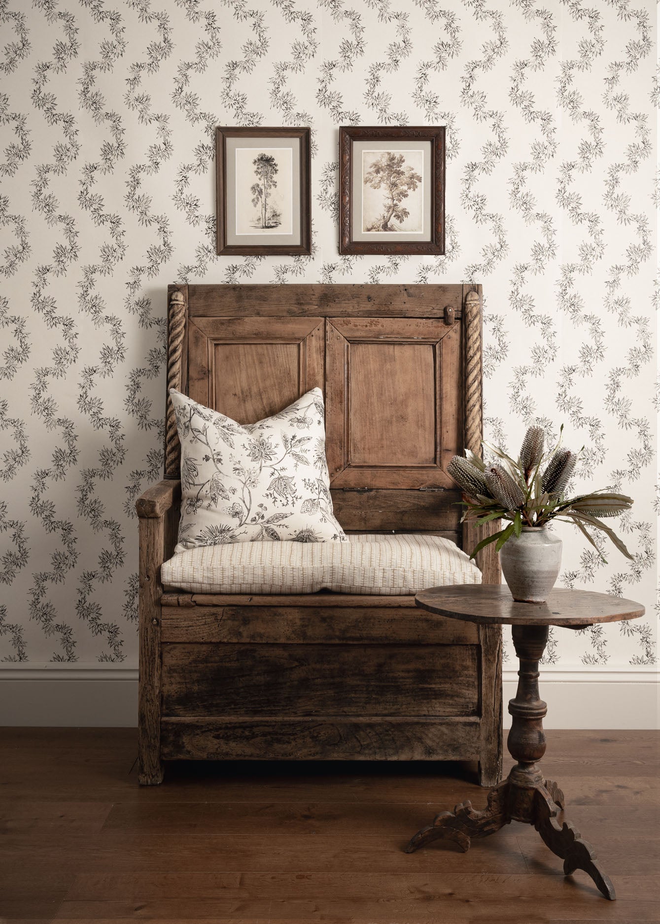 Wooden bench with floral cushion against a patterned wall with framed pictures.