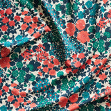Close up of gently draped printed linen fabric with a dense flower and leaf pattern in shades of coral, red, blue and turquoise on a white background.