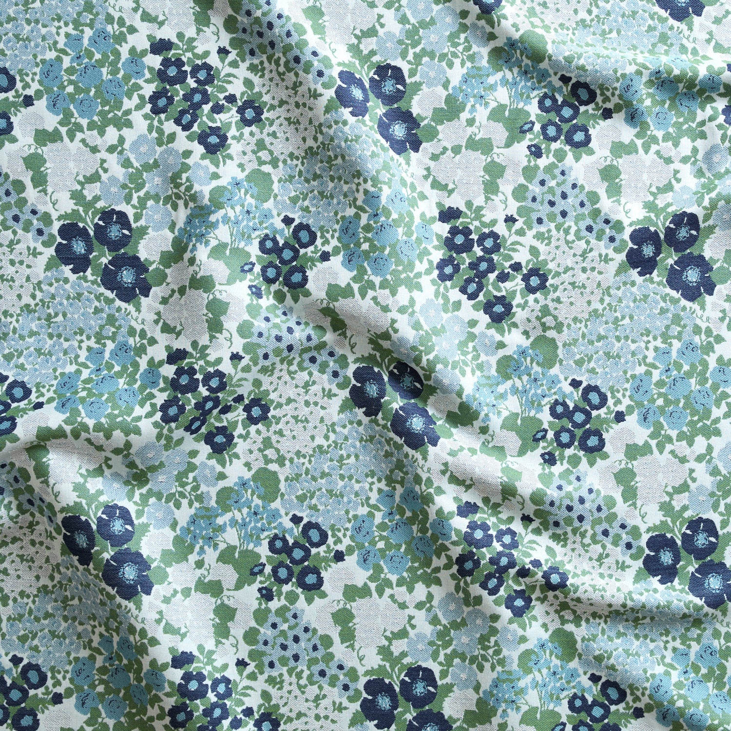 Close up of gently draped Indoor-Outdoor fabric with a dense flower and leaf pattern in shades of blue, green and white. 