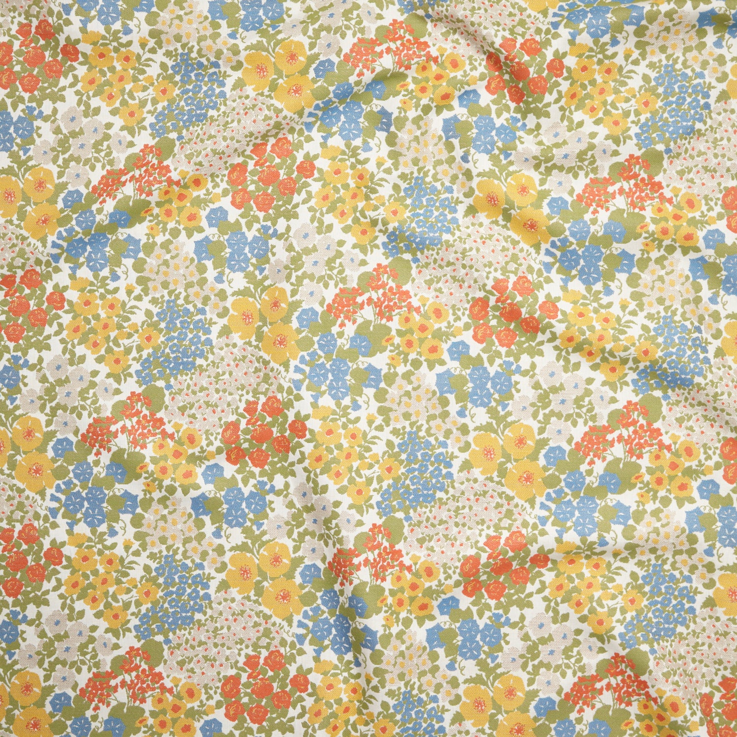 Close up of gently draped Indoor-Outdoor fabric with a dense flower and leaf pattern in shades of  yellow, orange, blue, green and white. 