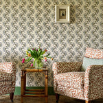 Living room scheme with orange and cream patterned chairs, sisal rug, rattan side table and a floral stripe wallpaper. 