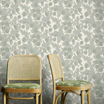 Two wooden chairs with green cushions against a floral-patterned wallpaper.