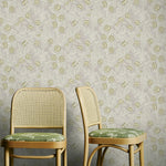 Two wooden chairs with green cushions against a yellow and grey floral patterned wallpaper.