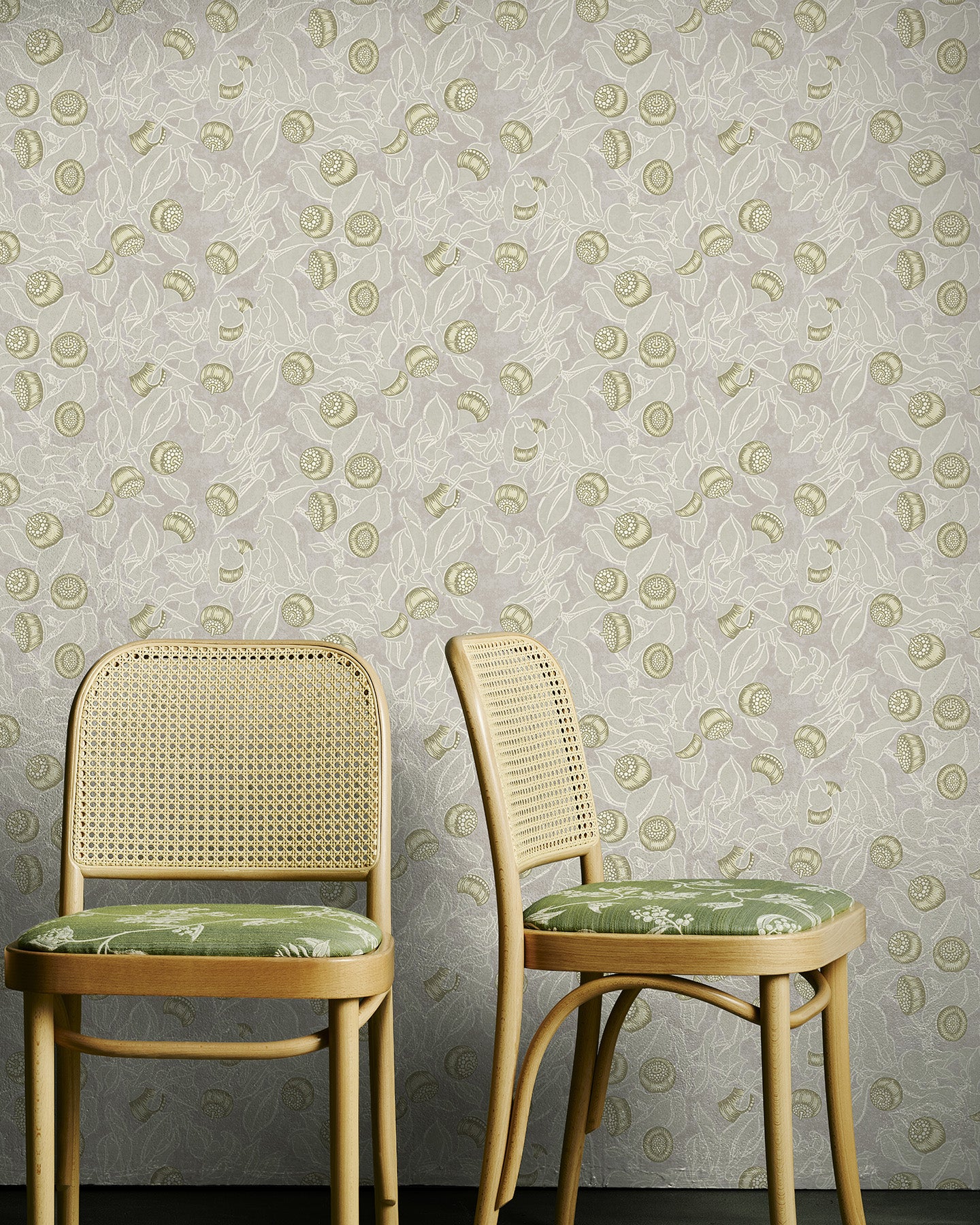 Two wooden chairs with green cushions against a yellow and grey floral patterned wallpaper.