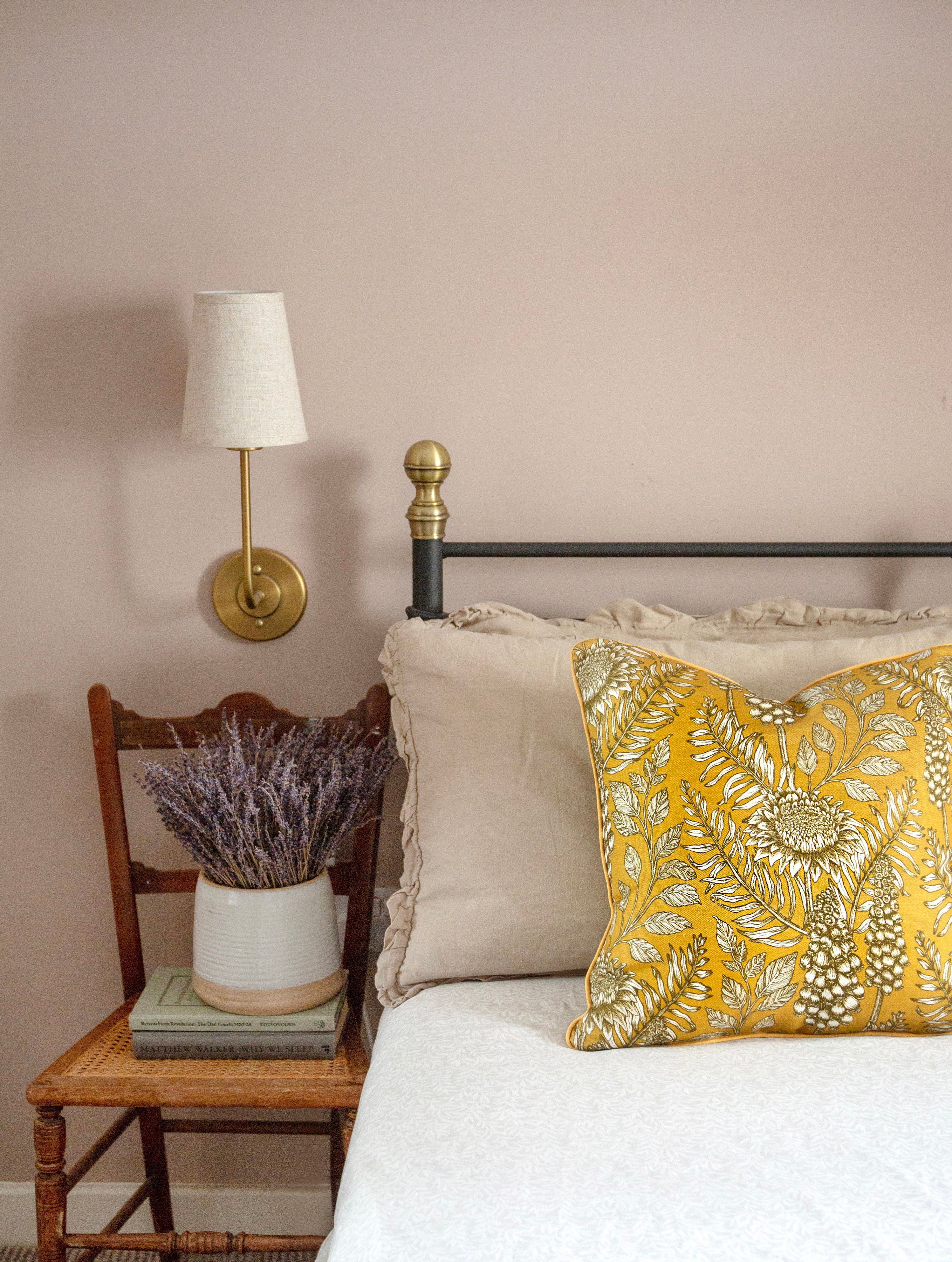A cozy bedroom tableau with flowers, books and a large throw pillow upholstered in floral fabric in black, white and yellow.