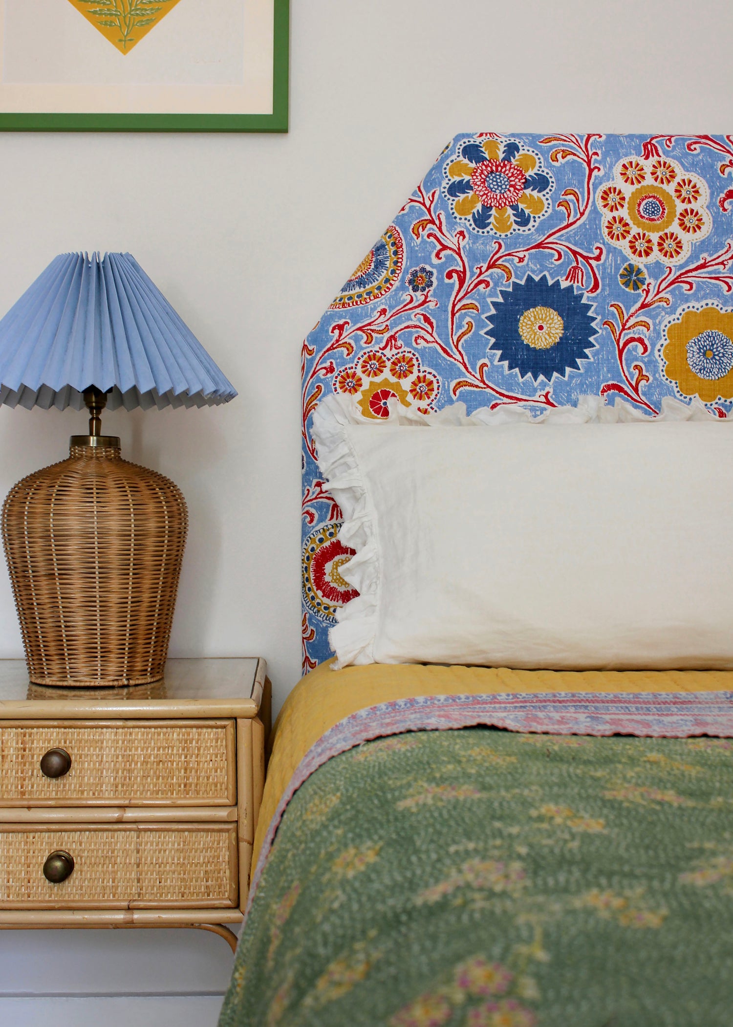Bedroom tableau with headboard upholstered in printed linen in a handdrawn playful floral design in red, yellow, green and blue on a light blue field.