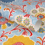 Wallpaper roll in a handdrawn playful floral design in red, yellow, green and blue on a light blue field.
