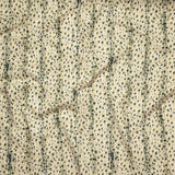 Close up of gently draped printed linen with small scale painterly animal print in dark green and tan on a beige background