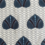 A close-up of a fabric pattern featuring repeating stylized fan-shaped motifs in dark blue, slate blue, and brown on a cream background with a fine repeating wave line pattern.