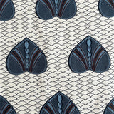 A close-up of a fabric pattern featuring repeating stylized fan-shaped motifs in dark blue, slate blue, and brown on a cream background with a fine repeating wave line pattern.