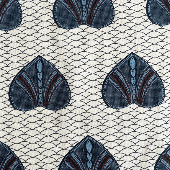 A close-up of a fabric pattern featuring repeating stylized fan-shaped motifs in dark blue, slate blue, and brown on a cream background with a fine repeating wave line pattern.
