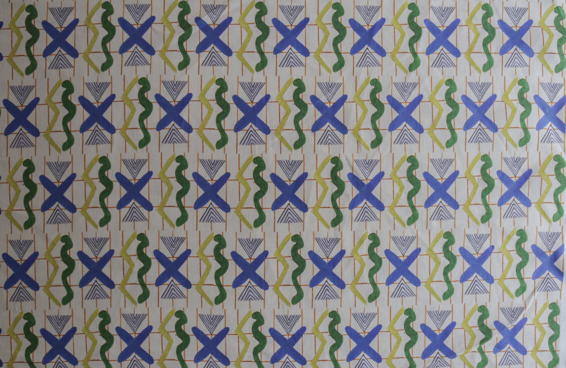 Close up printed fabric with green squiggles, white striped triangles, blue X marks on a broken grid in orange on a white background. 