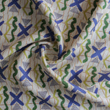 Close up of gently draped printed fabric with green, white triangles, blue X marks on a broken grid in orange on a white background. 