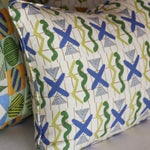 A close-up of a decorative throw pillow with a mid-century modern pattern featuring blue and green abstract shapes on a cream background, with other patterned pillows partially visible behind it.