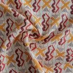 Close up of gently draped printed fabric with red squiggles, pink striped triangles, orange  X marks on a broken grid in orange on a white background. 